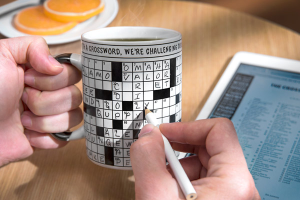 Man tackling a crossword puzzle on the surface of his coffee mug.