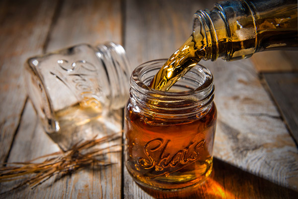 A miniature mason jar being filled with a shot of liquor.